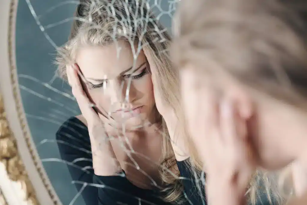 Broken mirror reflection of a young woman looking at herself mirrors reflection - self-acceptance and healing.