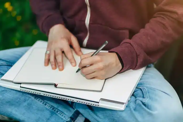 Thoughtful person writing in an open notebook outdoors, symbolizing reflection and peace.