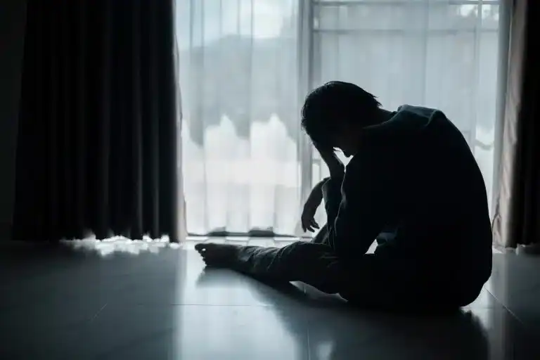 Lonely person sitting on the floor, feeling distressed or overwhelmed, near a window with curtains.