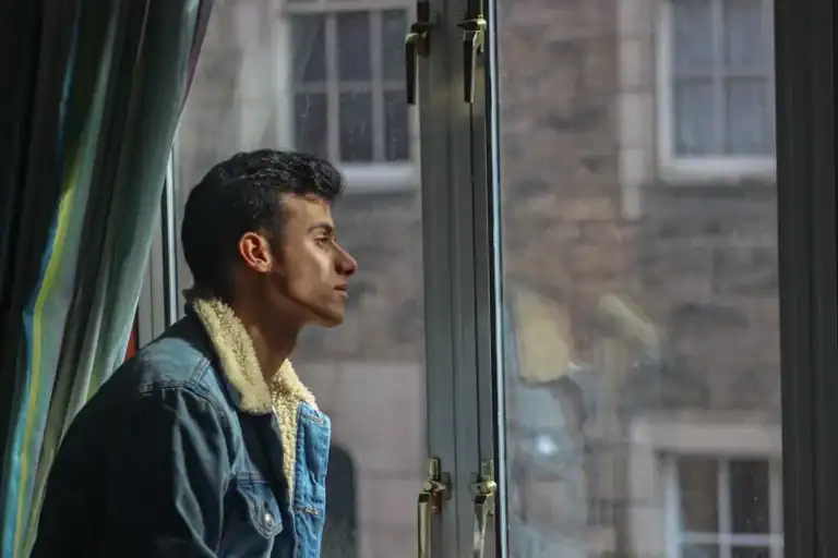 Man in a jacket looking out a window in contemplation