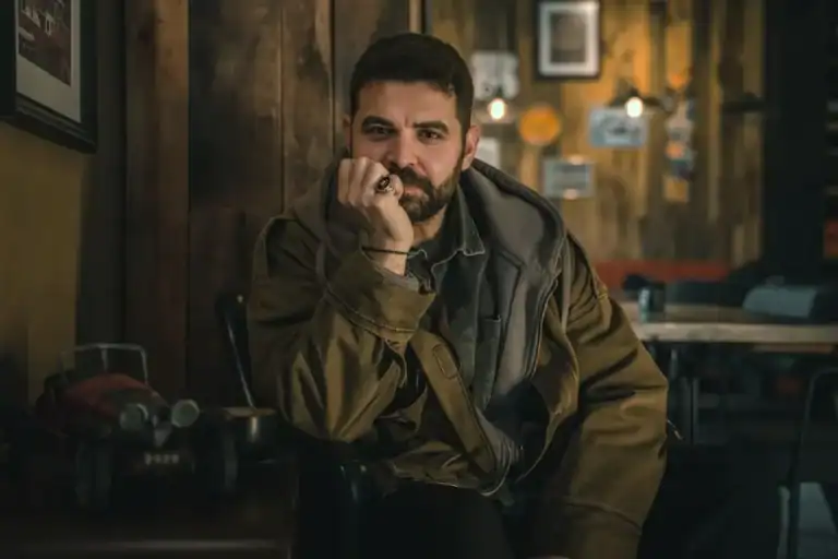 Man sitting alone in a dimly lit room, hand on chin, deep in thought